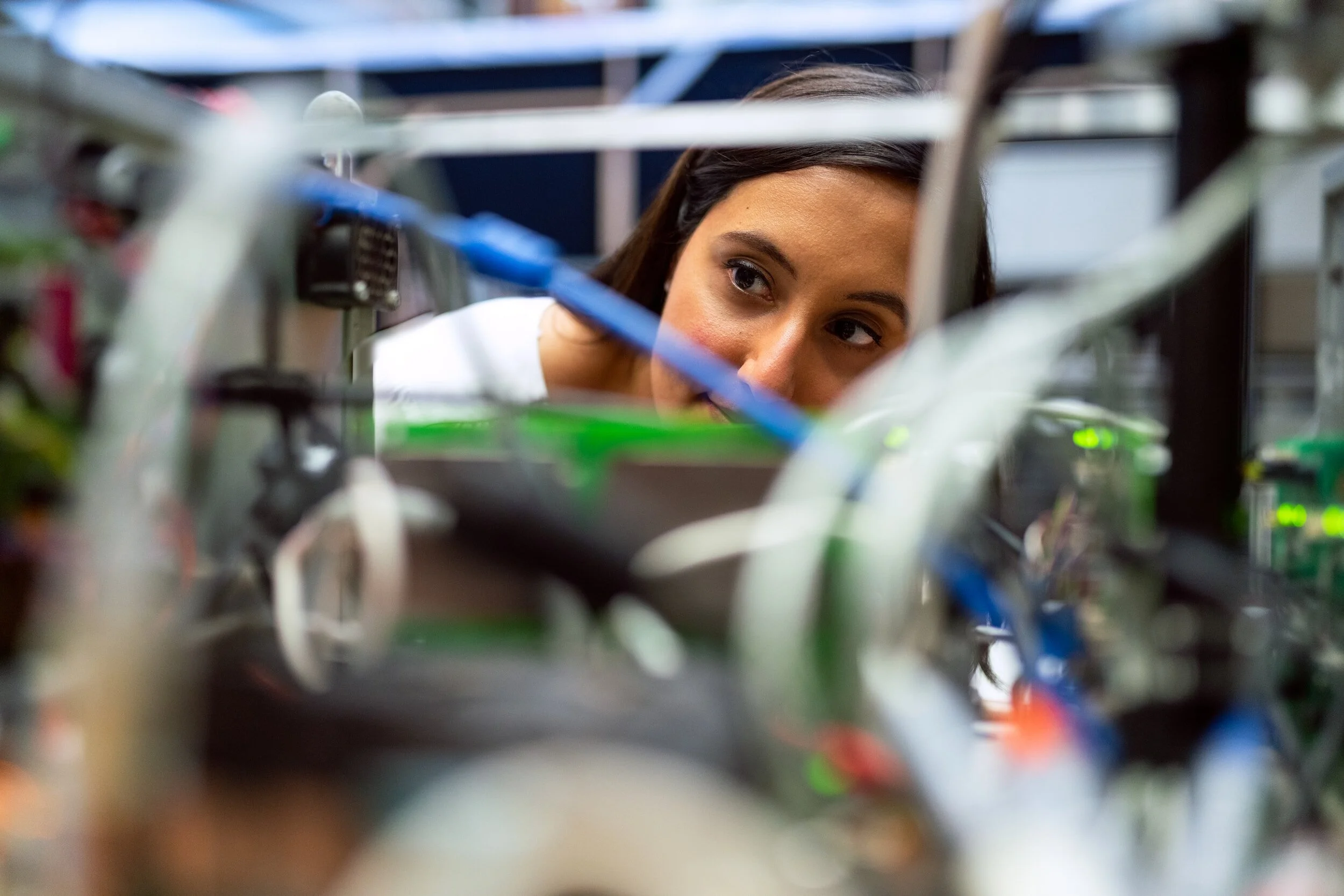 A woman with dark hair looking through electronic equipment with wires and circuit boards.