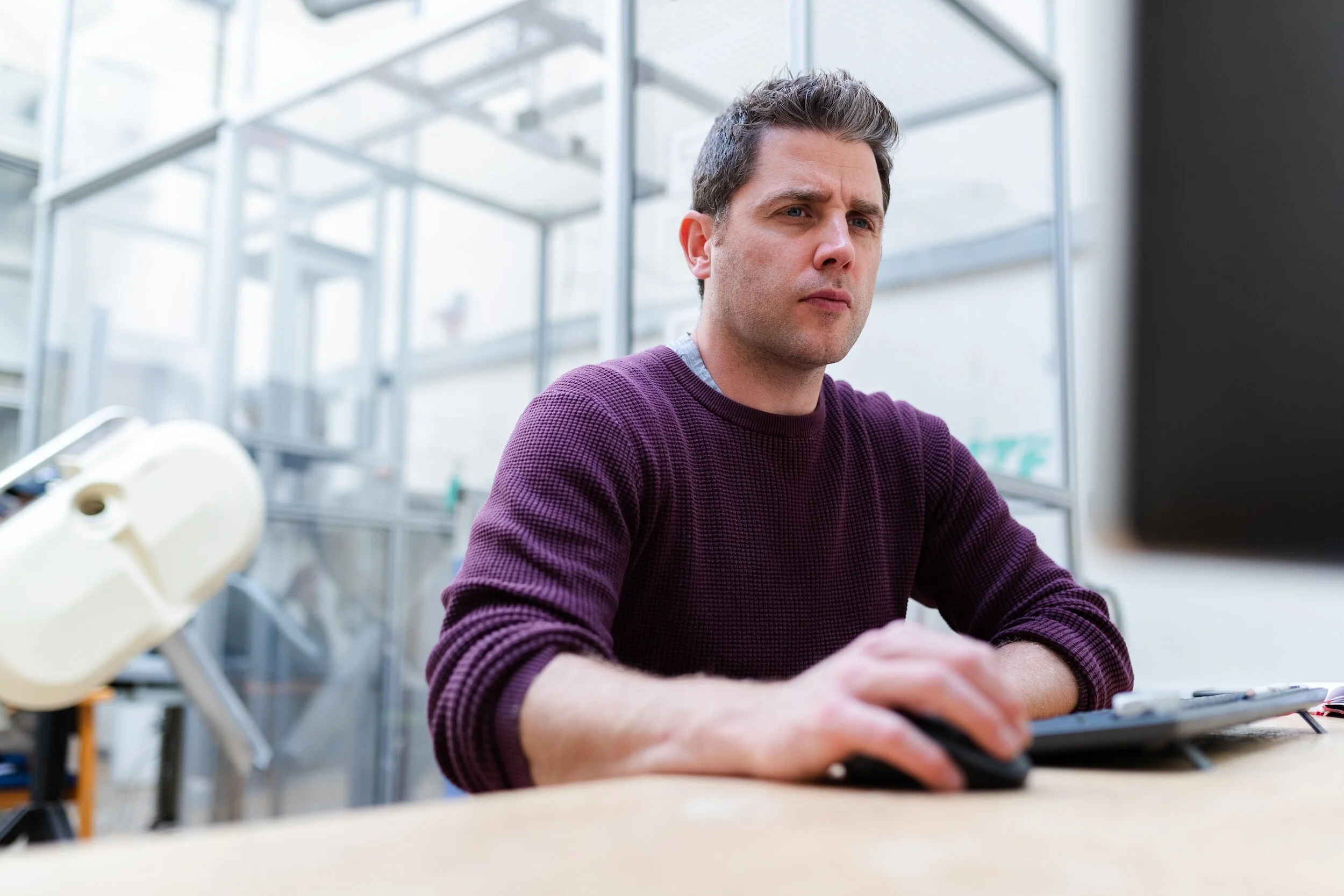 A man working at a desk in a modern office setting, focused on his computer screen.