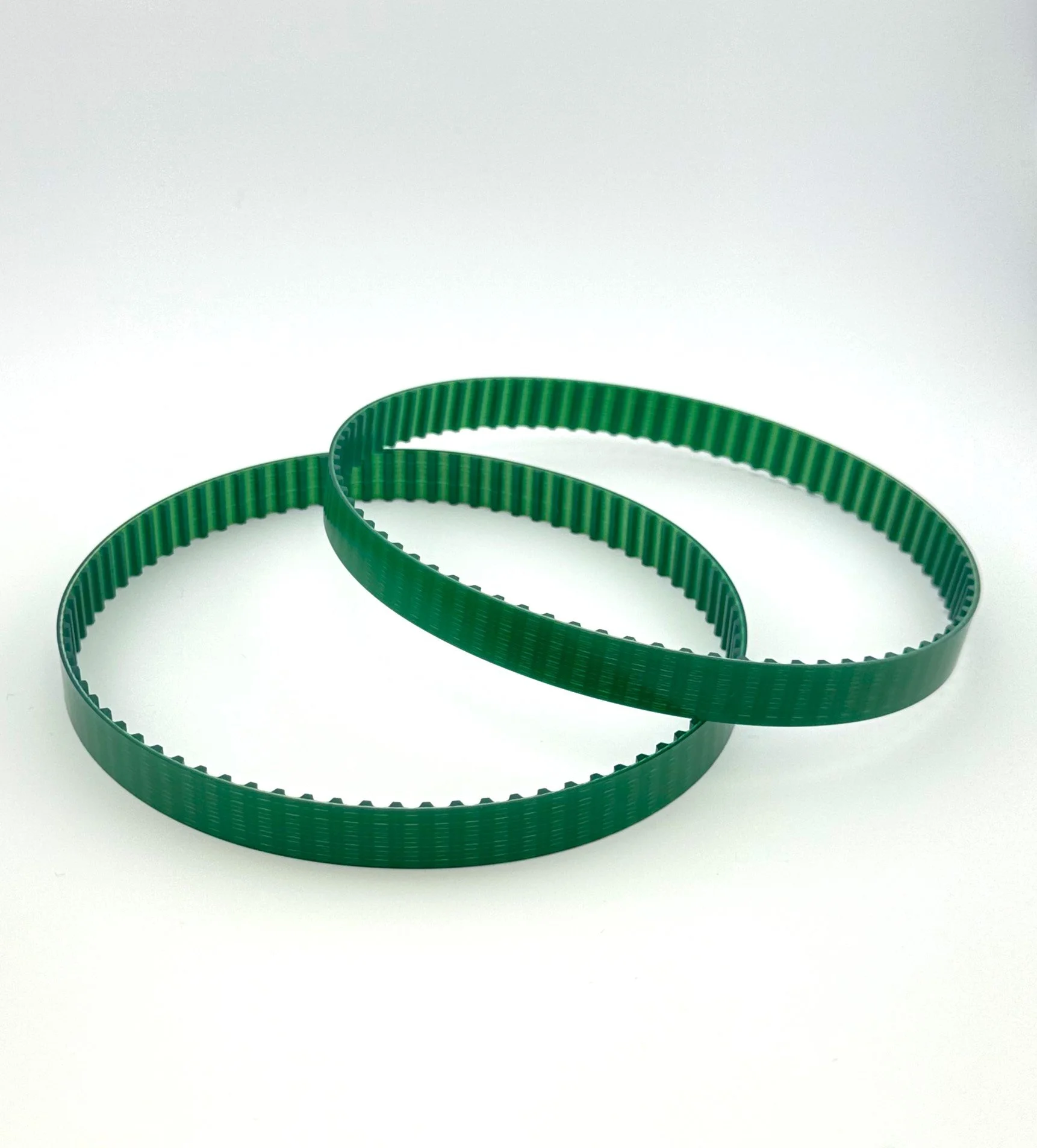 Two green plastic timing belts placed on a white background.