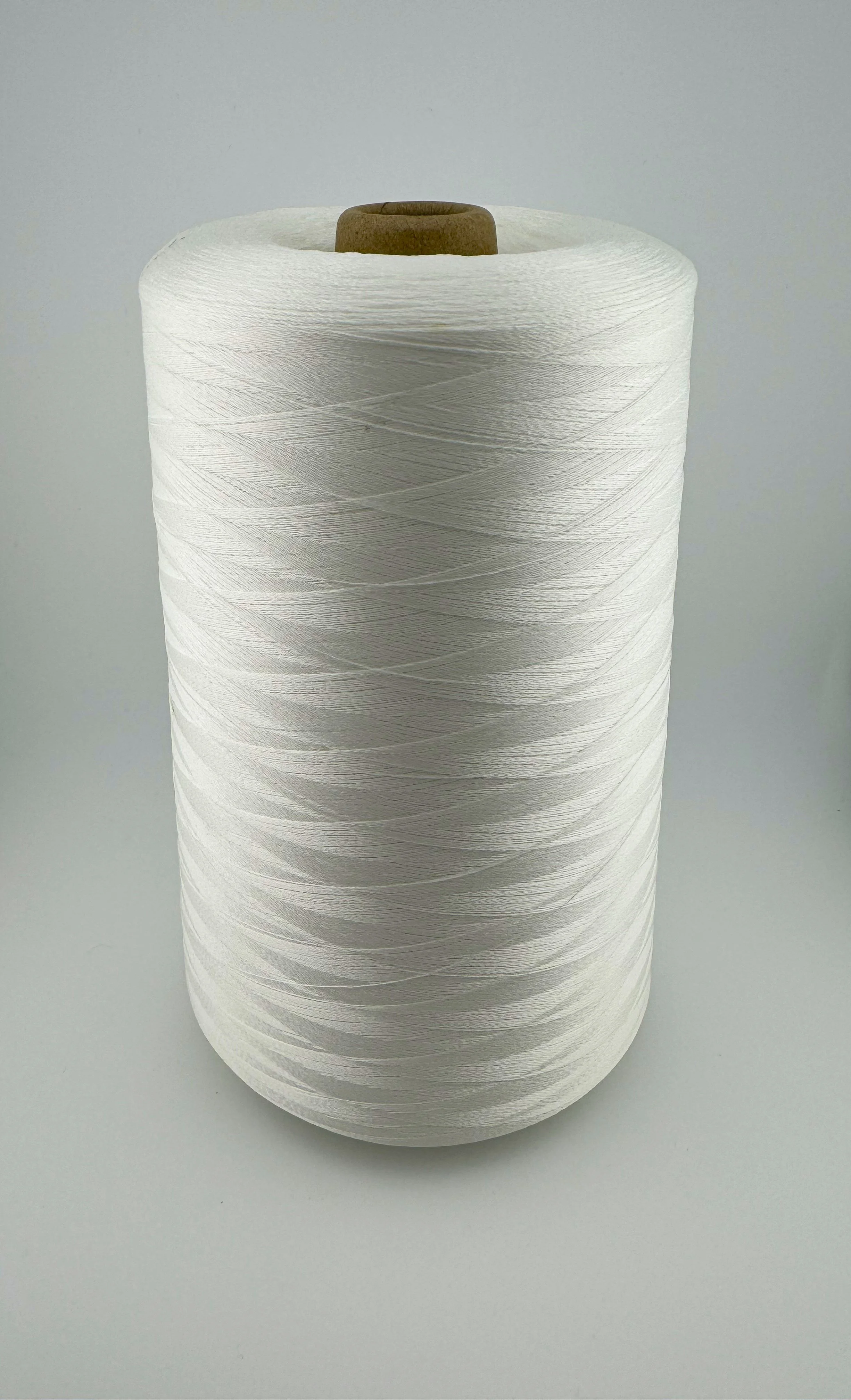 A large spool of white sewing thread standing upright on a plain light gray surface.
