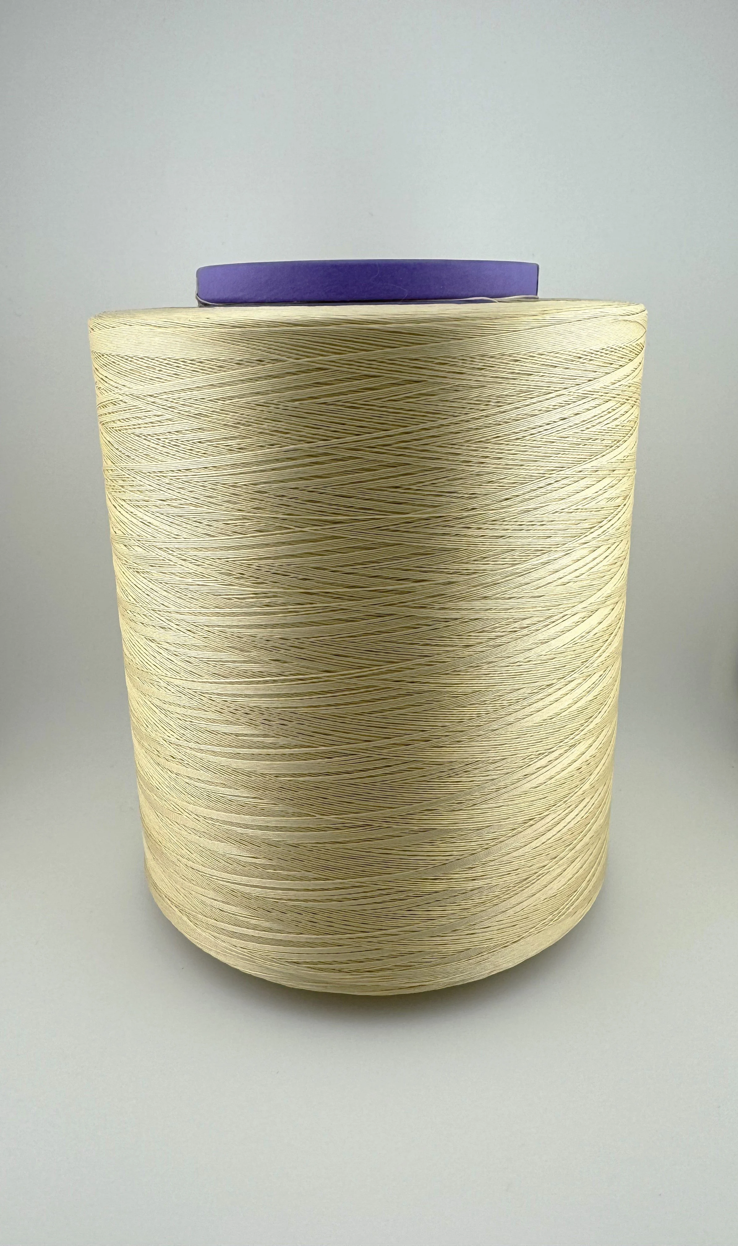 A large spool of beige thread with a purple top, sitting on a plain white surface against a light gray background.